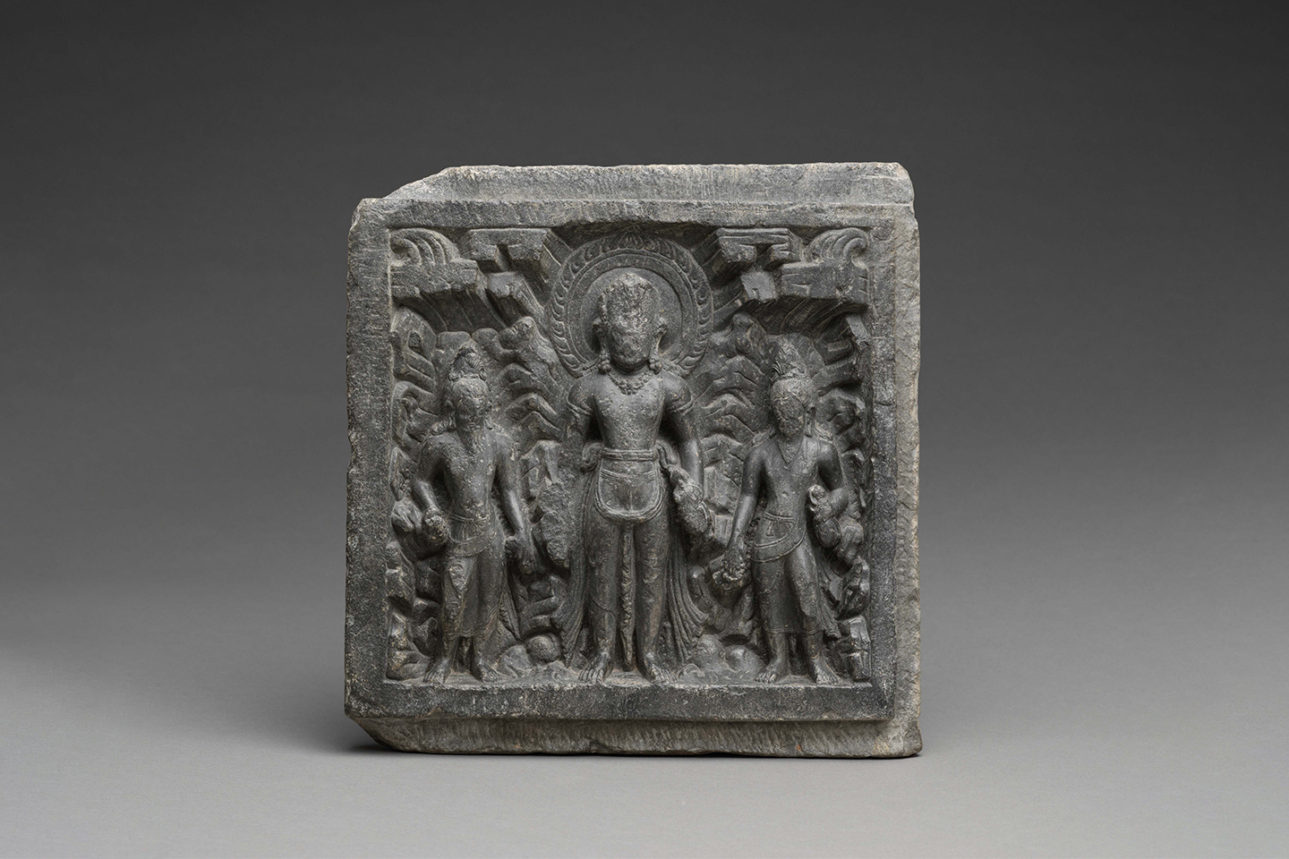 A grey square shaped stone with an engraved scene photographed against a grey background.